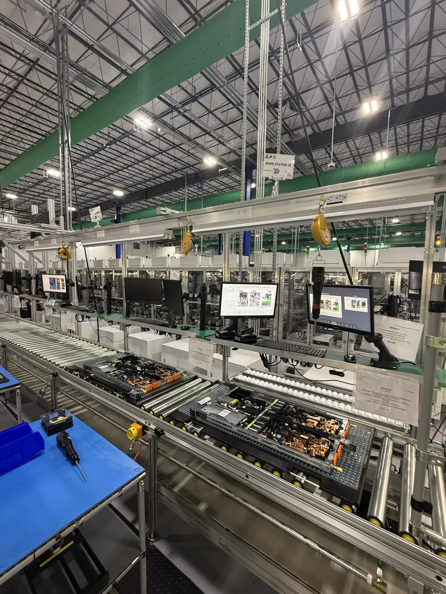 Assembly workstation with roller conveyor, monitors, and tool balancers